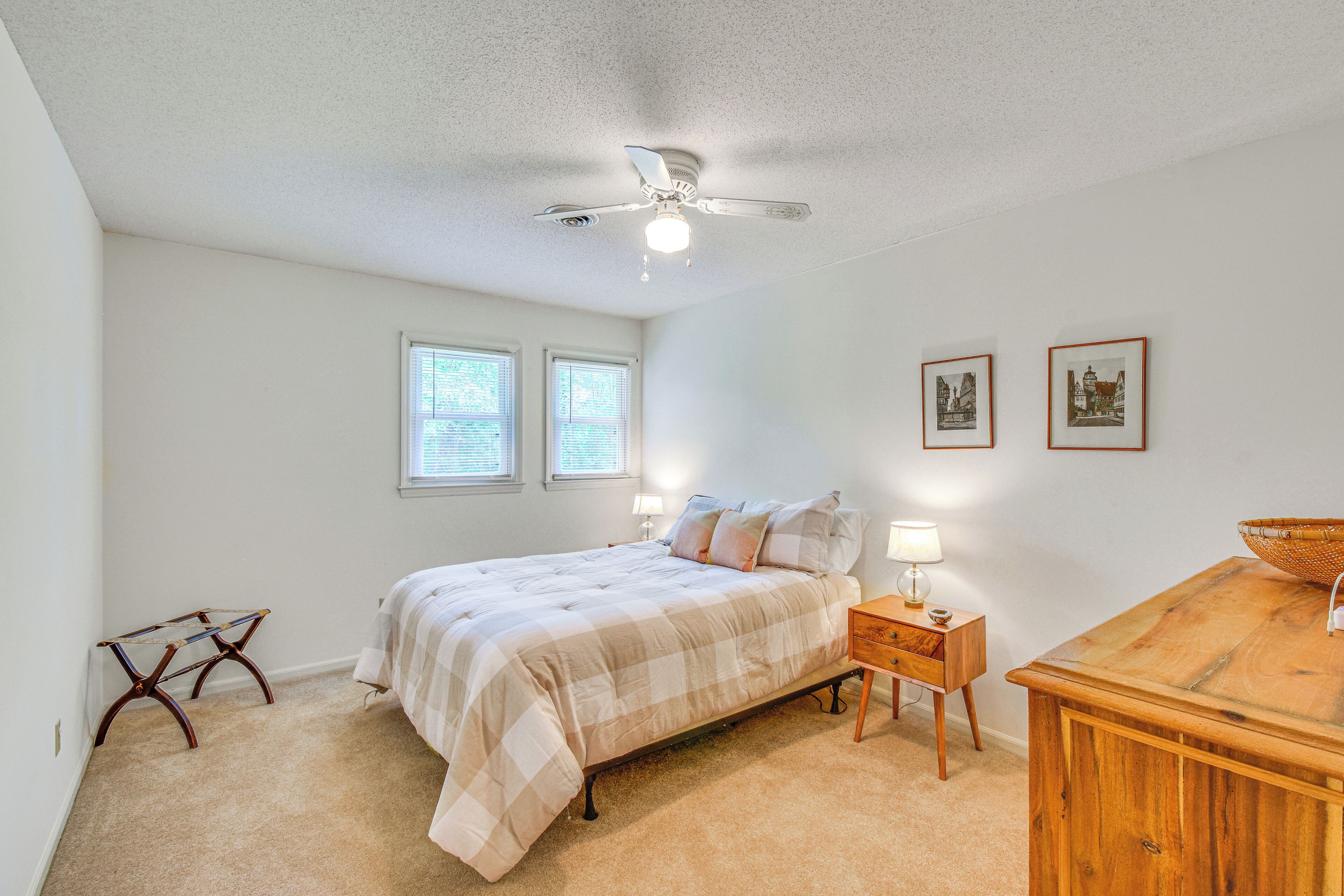 A bedroom with a bed, bedside tables, a wooden dresser, a ceiling fan, and two windows.