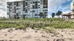A multi-story building with numerous balconies, a sandy foreground with vegetation, and a clear sky. - Oceanfront Fort Pierce Condo: Pool & Beach Access! (Fort Pierce)