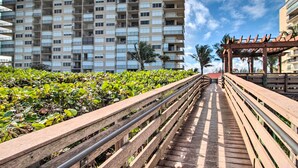 A wooden boardwalk leading to a high-rise building with balconies, surrounded by greenery. - Oceanfront Fort Pierce Condo: Pool & Beach Access! (Fort Pierce)