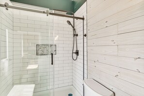 A modern bathroom with white tiled walls, a glass shower enclosure, and a wooden panel accent.