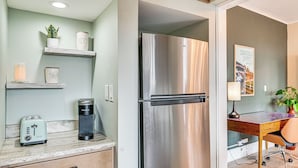 Une cuisine moderne équipée d’un réfrigérateur en acier inoxydable, d’une machine à café et d’un grille-pain. On y trouve des étagères ornées d’objets décoratifs et un tableau encadré accroché au mur.