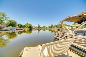 Une rivière paisible où des bateaux sont amarrés sur la rive droite, une chaise blanche au premier plan et des bâtiments le long de la berge.