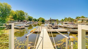 Een houten steiger die leidt naar een jachthaven met boten en een overdekt zitgedeelte.