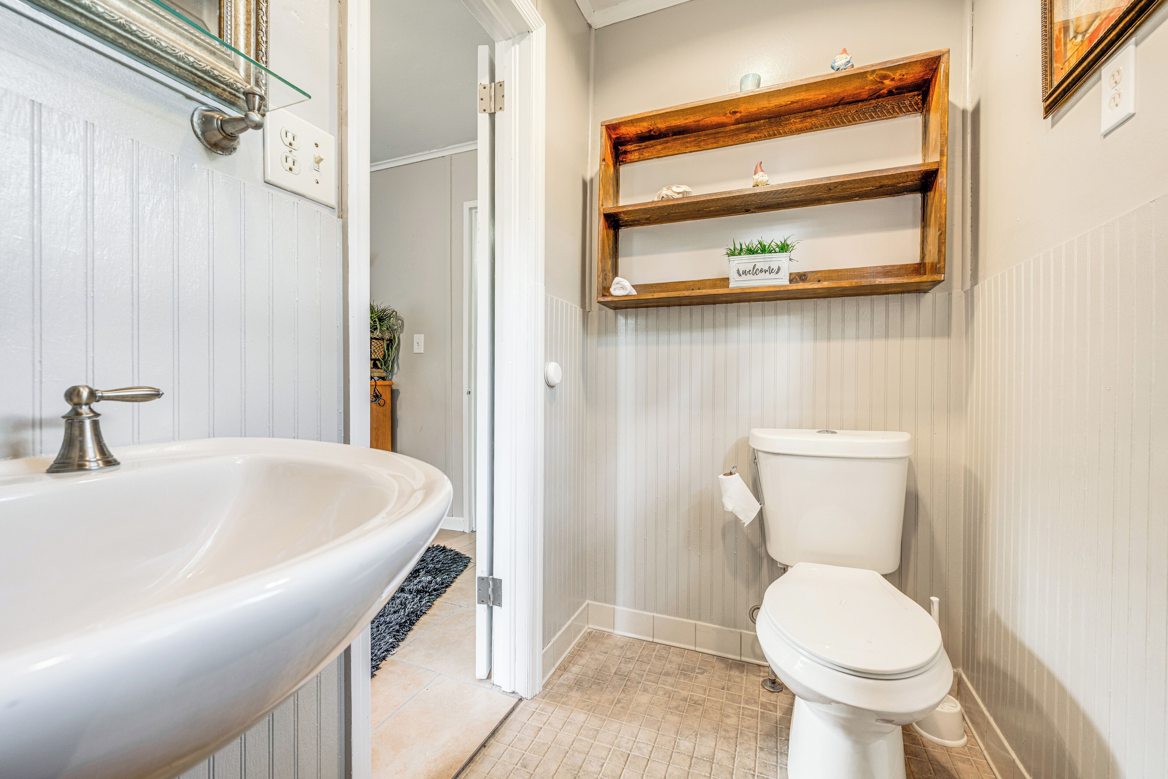 A bathroom with a white sink, a toilet, and wooden shelves above the toilet.