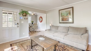 Un salon avec un canapé beige, une table basse en bois, un tapis à motifs, une porte avec une fenêtre, un ventilateur de plafond et un tableau encadré au mur.
