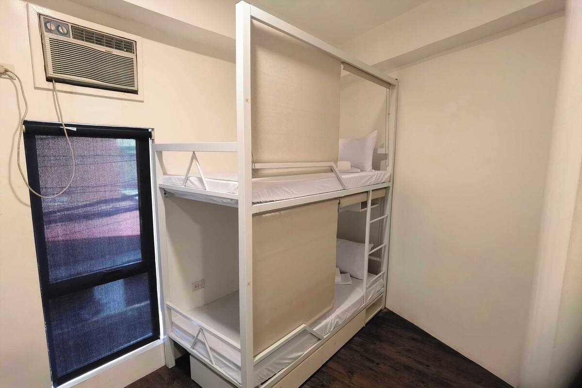 A bunk bed room with a window, a heater, and a power outlet.
