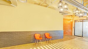 A spacious indoor area with a brick wall, two orange chairs, and a patterned floor. - Spot On Hostel ,Taguig Manila Formerly MYTOWN HongKong (Taguig)