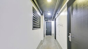 A narrow hallway with a concrete floor, a window with horizontal blinds, and a door at the end. - Spot On Hostel ,Taguig Manila Formerly MYTOWN HongKong (Taguig)