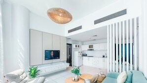 Un salon moderne doté d’un téléviseur à écran plat, d’un canapé, d’une table basse et d’un coin cuisine avec des meubles blancs et une cuisinière.