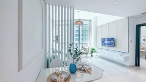 Un espace repas moderne avec une table blanche, des chaises et une table avec un plateau en verre. Un téléviseur est fixé au mur et une plante décorative est posée sur la table.