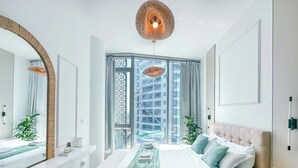 Une chambre moderne avec un grand lit, une table de chevet, un miroir et une vue sur un immeuble par la fenêtre.