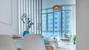 Un espace repas moderne avec des chaises blanches, une table ronde et une grande fenêtre donnant sur le paysage urbain.