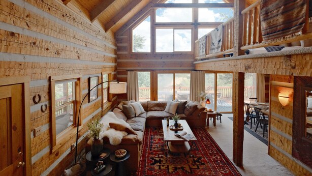 A log cabin interior with a wooden ceiling, large windows, a living room with a sofa and coffee table, and a dining area with chairs and a table. - Hillside Cabin - Mt Views - Patio Decks - Hot Tub (Cascade)