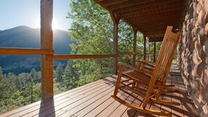 A wooden rocking chair on a wooden deck with a stone wall, overlooking a forested valley. - Hillside Cabin - Mt Views - Patio Decks - Hot Tub (Cascade)