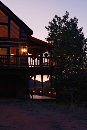 A two-story wooden building with a balcony, large windows, and a view of the landscape.