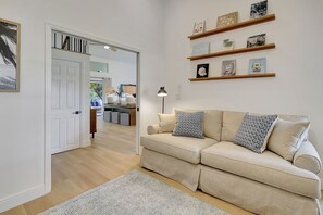 Una sala de estar con un sofá color crema, un tapete estampado y una estantería con diversos objetos.