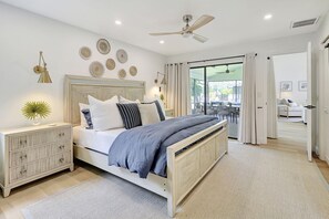 Un dormitorio moderno con cama, mesitas de noche, ventilador de techo y vistas al exterior.