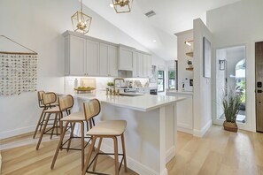 Una cocina moderna con armarios blancos, una isla central con taburetes altos e iluminación colgante.