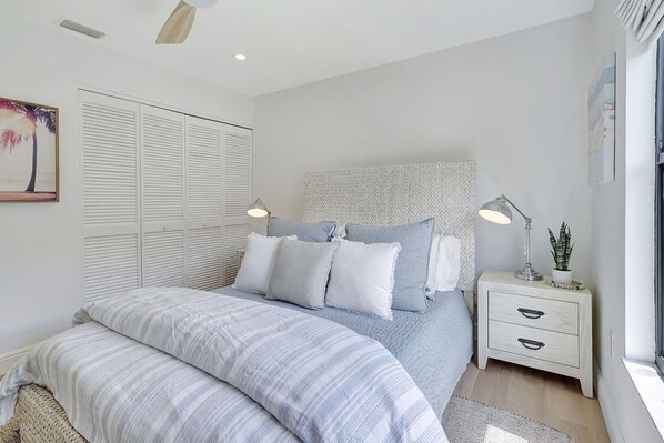 A bedroom with a bed, bedside tables, a nightstand, a window, and a wall-mounted headboard.