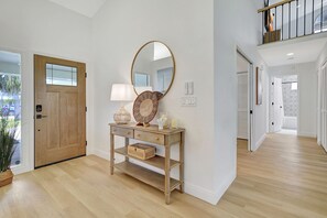 A hallway with a wooden door, a console table with decorative items, a large mirror, and a staircase.