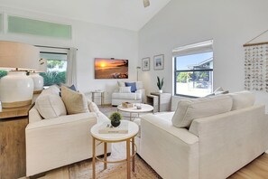 A modern living room with a sofa set, a coffee table, and a side table. There is a large window with a view of the outdoors.