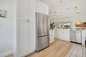 A modern kitchen with white cabinetry, stainless steel appliances, and pendant lighting.