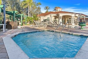 A swimming pool with lounge chairs and a covered area, surrounded by trees and a building with a tiled roof. - Amazing 3BR Home w Balcony very close to Disney! (Kissimmee)