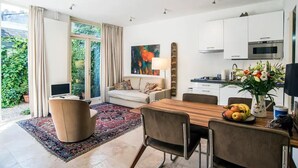 Una cocina moderna con armarios blancos, horno empotrado y microondas. Hay una zona de comedor con mesa y sillas de madera, y un amplio ventanal con cortinas.