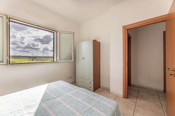 A bedroom with a bed, a wardrobe, a window with a view, and a door leading to another room.