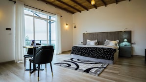 Une chambre avec un grand lit, un bureau avec un ordinateur portable, une chaise, une table de chevet avec une lampe et une vue par la fenêtre.
