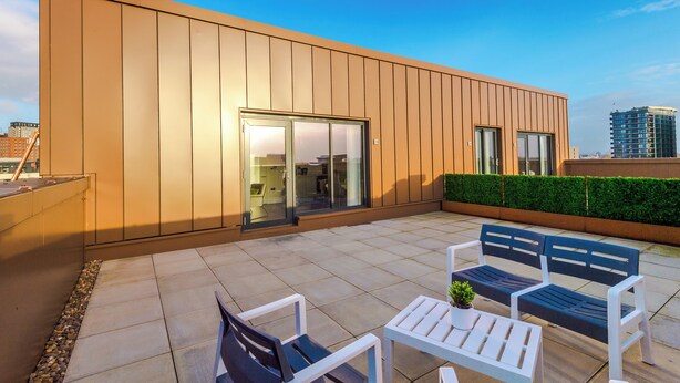 A modern building with a flat roof, large glass windows, and a patio area with outdoor seating.