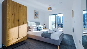 A modern bedroom with a large wardrobe, a neatly made bed, and a city view through large windows.