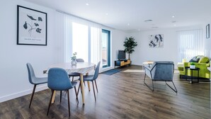A modern living room with a dining area, a sofa, a TV, and a plant.