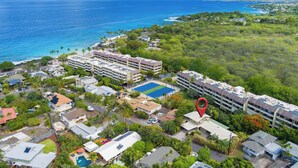 An aerial view of a coastal hotel with multiple buildings, a swimming pool, and a view of the ocean. - Magic Sands Light Hawaii Oasis: Steps to Beach, AC (Kailua Kona)
