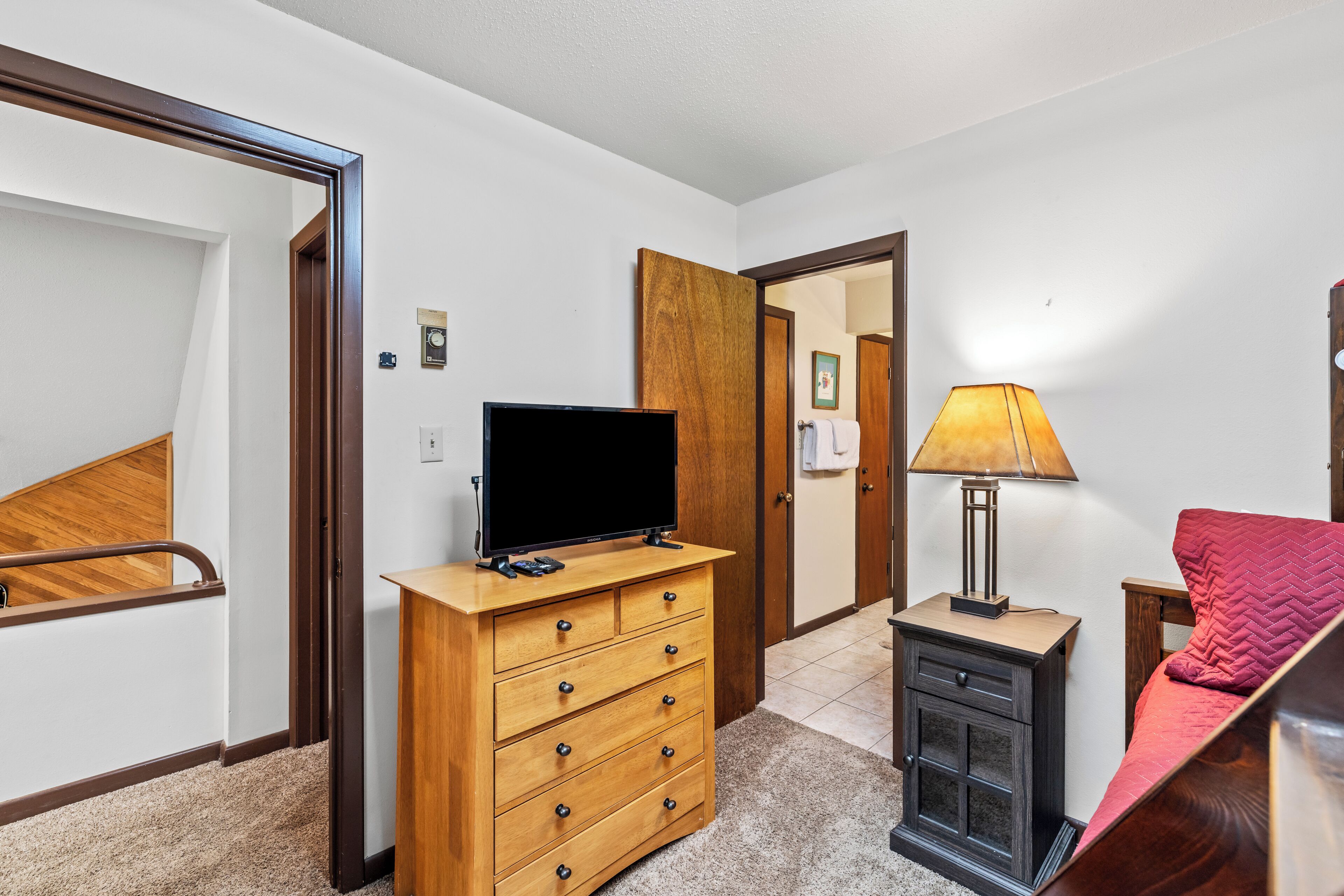 Une chambre à coucher avec une commode en bois, une télévision, une lampe et un lit.
