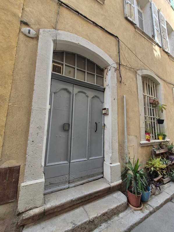 A building with a large grey double door, a small window with shutters, and potted plants on the ground level.