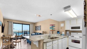 Una cocina moderna con una isla central, armarios blancos y vista al océano.