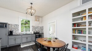 Une cuisine moderne avec un plancher en bois foncé, un îlot central et une bibliothèque blanche remplie de livres et d’objets décoratifs.