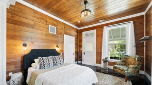 Une chambre avec un plafond en bois, un lit avec une literie à motifs, une chaise et une fenêtre avec des rideaux.