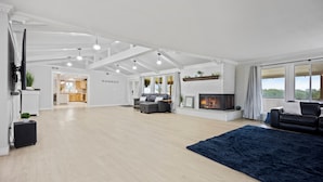 A spacious living room with a fireplace, a dark blue rug, and a kitchen in the background. - 5BR Retreat On Acreage Near KC (Liberty)