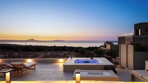 Una terraza en la azotea con jacuzzi, sillones de descanso y vistas al mar al atardecer.