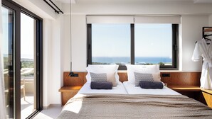 Un dormitorio moderno con una cama grande, dos almohadas, una mesita de noche y vistas al mar a través de un ventanal amplio.