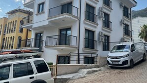 Un immeuble à plusieurs étages doté de balcons, d’une allée pavée et de véhicules stationnés.