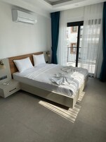 Habitación de hotel moderna con una cama grande, una mesita de noche, equipo de aire acondicionado y vistas al balcón exterior.