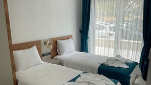 Une chambre d’hôtel avec deux lits, chacun recouvert d’une courtepointe blanche et turquoise, doté d’une tête de lit en bois et agrémenté d’une table de chevet avec une lampe.