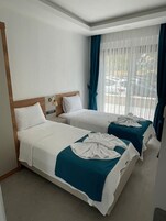 Habitación de hotel con dos camas, cada una con colcha blanca y azul turquesa, cabecero de madera y mesita de noche con lámpara.