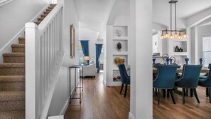 Ein modernes Interieur mit einer Treppe, einem Essbereich mit blauen Stühlen und einer Küche im Hintergrund.