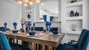 Comedor con una mesa de madera dispuesta para seis personas, sillas azules y jarrones decorativos azules.