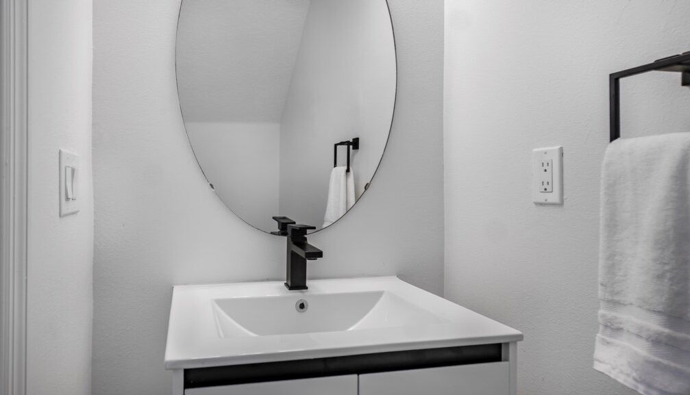 A bathroom with a white sink, a round mirror, and a towel hanging on a rack.