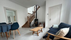 Uma sala de estar espaçosa com escada de madeira, área de jantar com mesa e cadeiras, e sofá com almofadas.